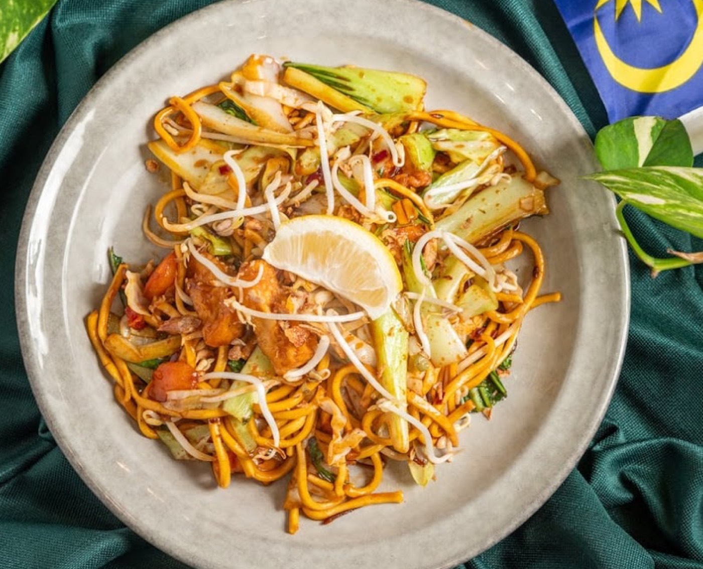 Mee goreng noodles with pak choi, bean sprouts and lemon on a stone plate